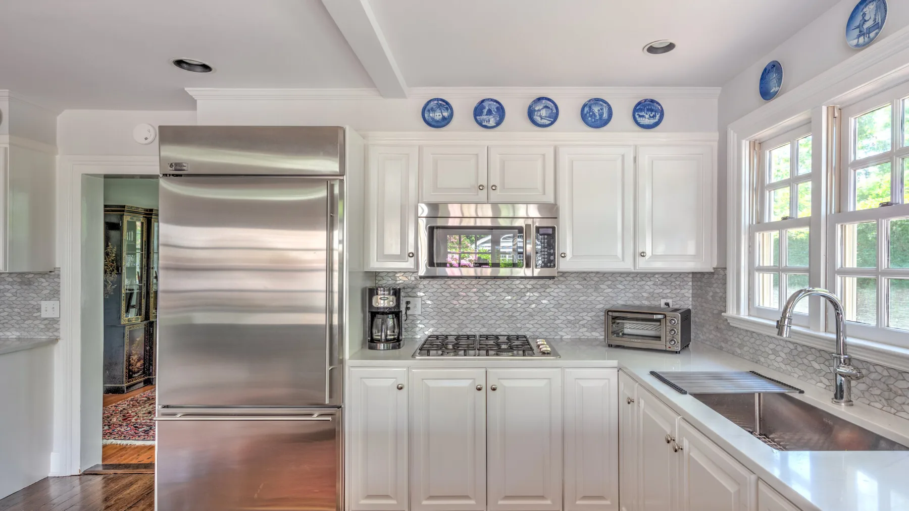 A bright kitchen with white cabinets, stainless steel appliances, and a large window.