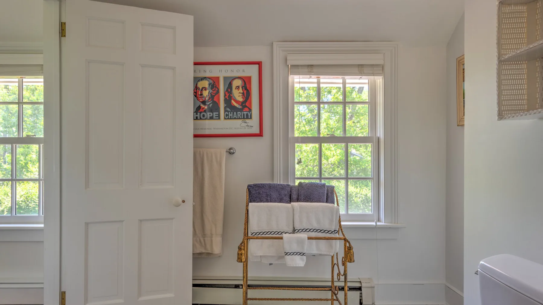 A bright room has a window, a chair with folded towels, and an open door.