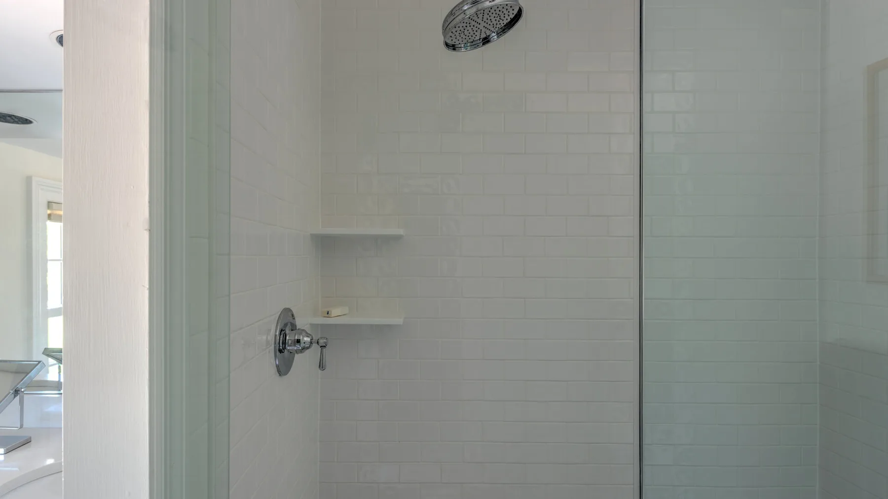 A tiled shower with a wall-mounted showerhead and shelves.