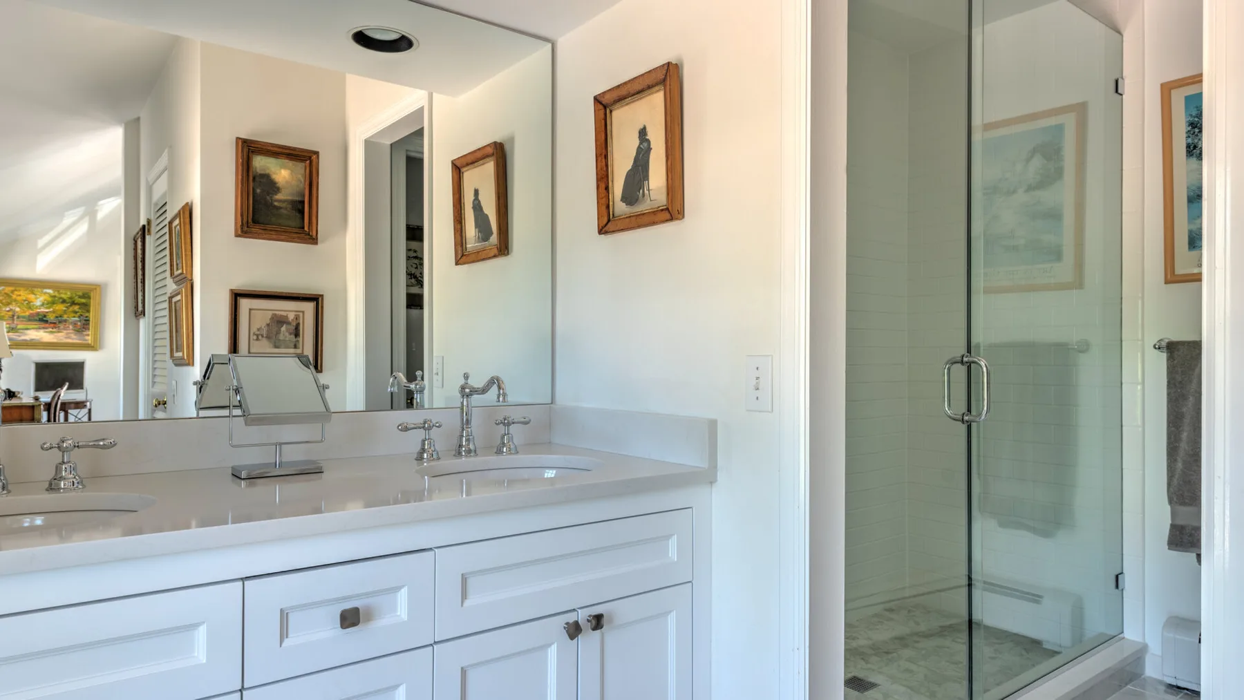 A bright bathroom vanity with a long counter and a glass shower.