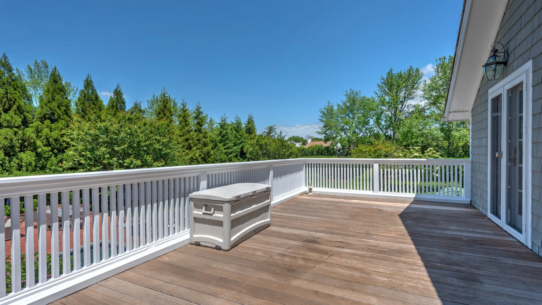 A spacious wooden deck overlooks green trees beneath a clear blue sky.