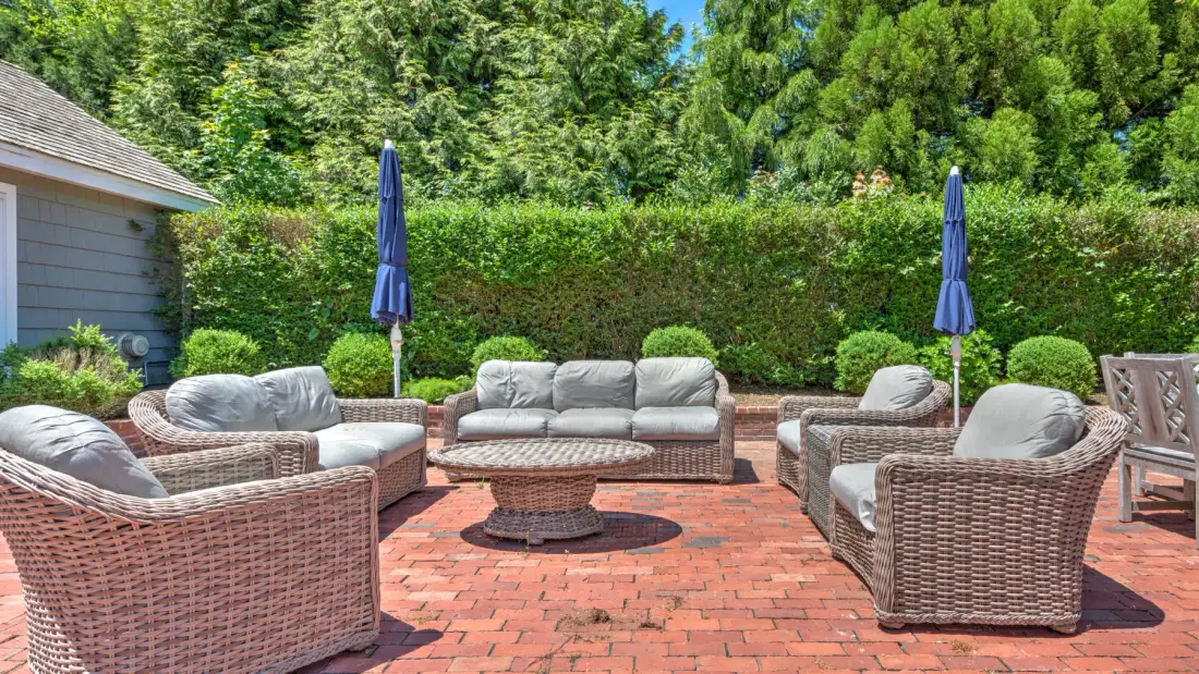 An outdoor patio has wicker seating, a low table, and closed umbrellas.