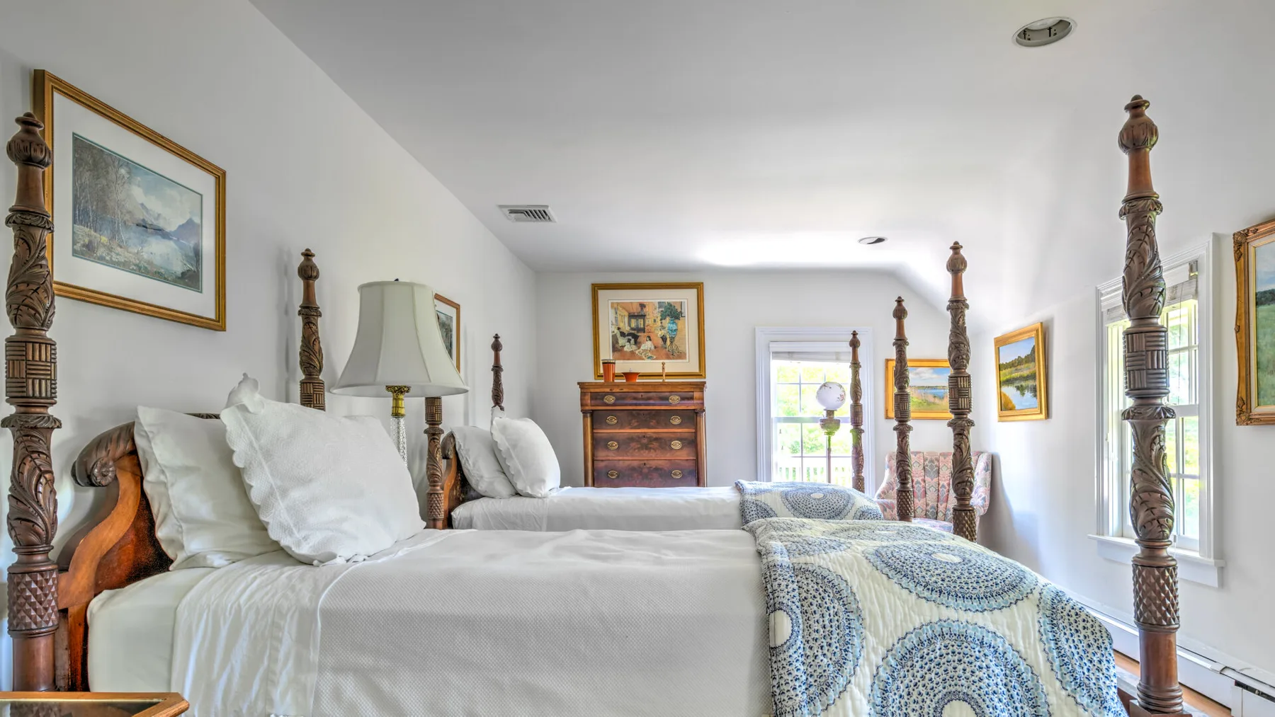 A bright bedroom with white bedding, carved bedposts, and framed artwork.