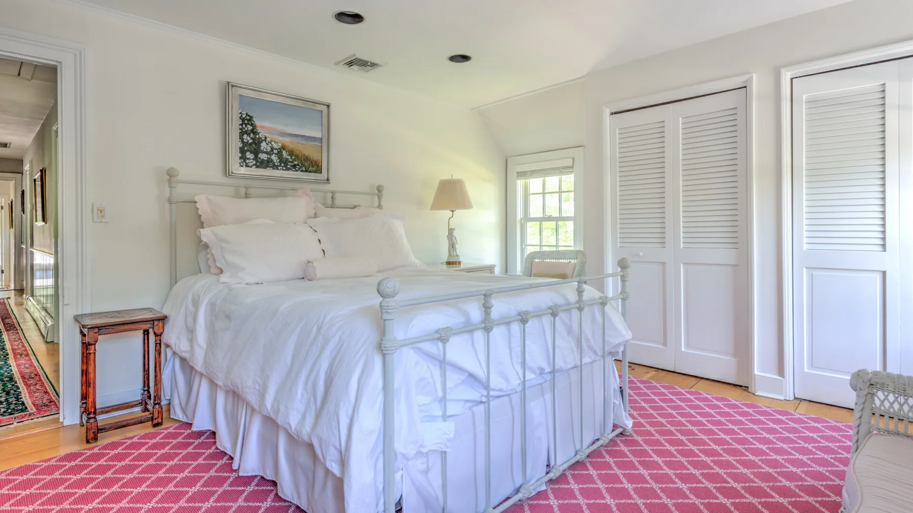 A bright bedroom with a white bed and pink patterned carpet.
