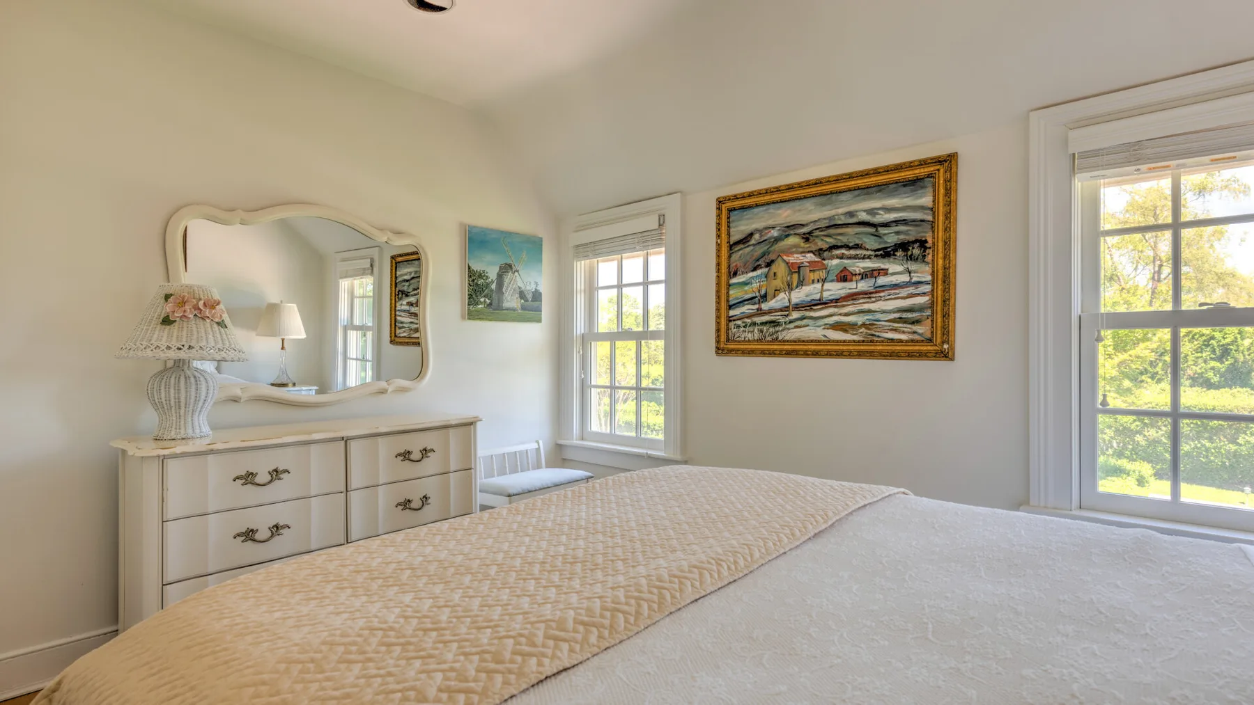 A bedroom with a patterned bedspread, dresser, and paintings on the wall.