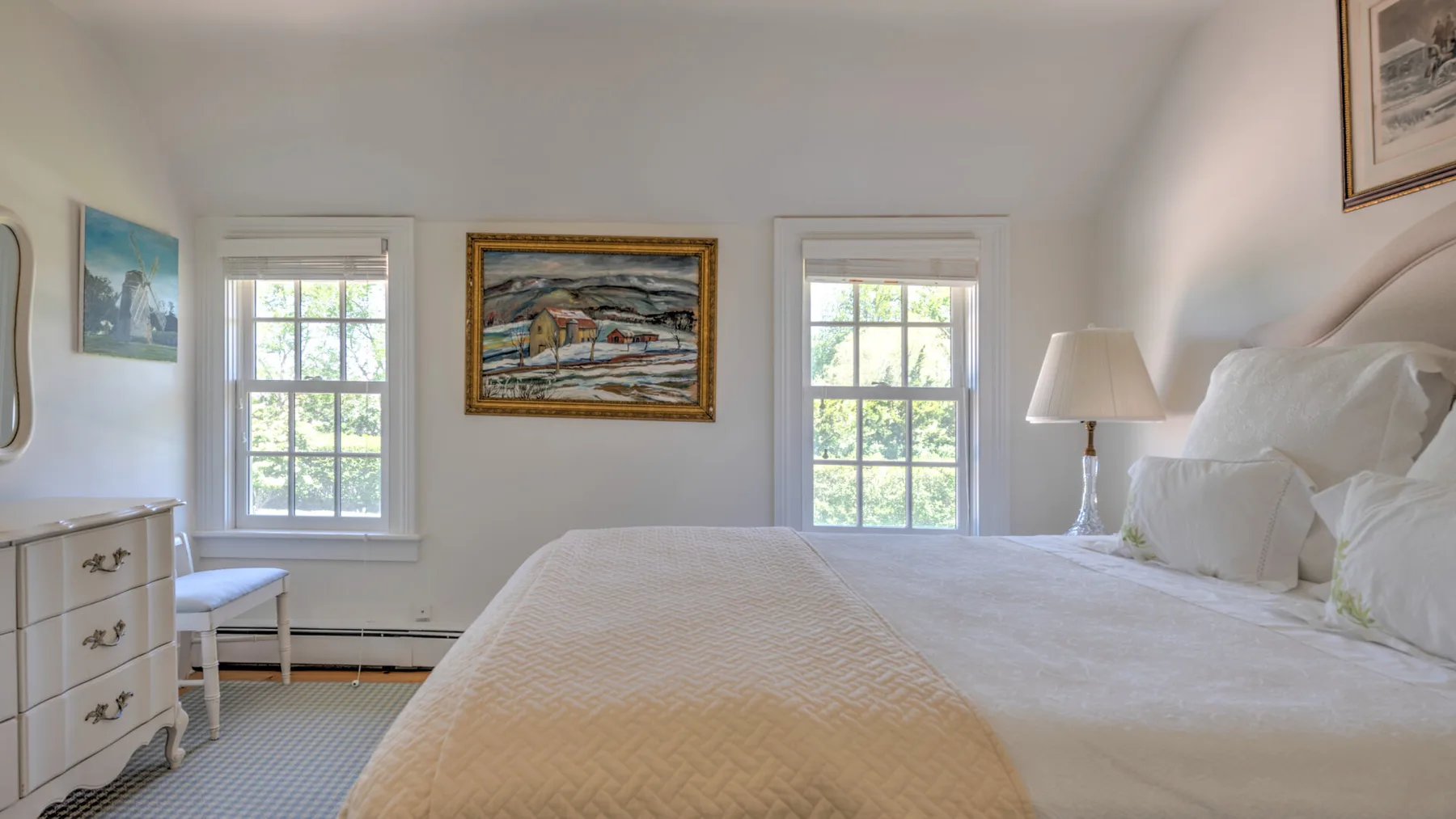 A bright bedroom with a neatly made bed and windows along the wall.