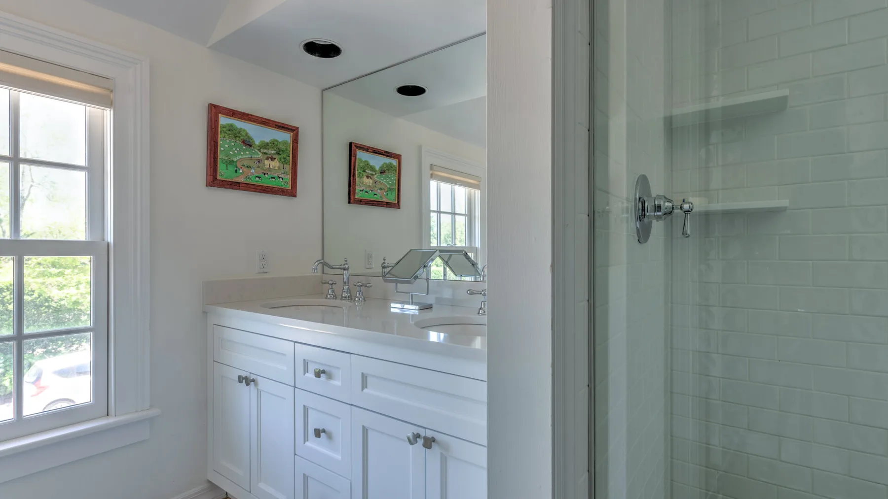 A bright bathroom with a white vanity, large mirror, and tiled shower.