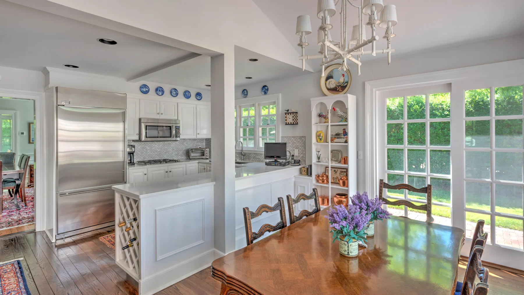 A bright dining area opens onto a kitchen, with a wooden table and large windows.