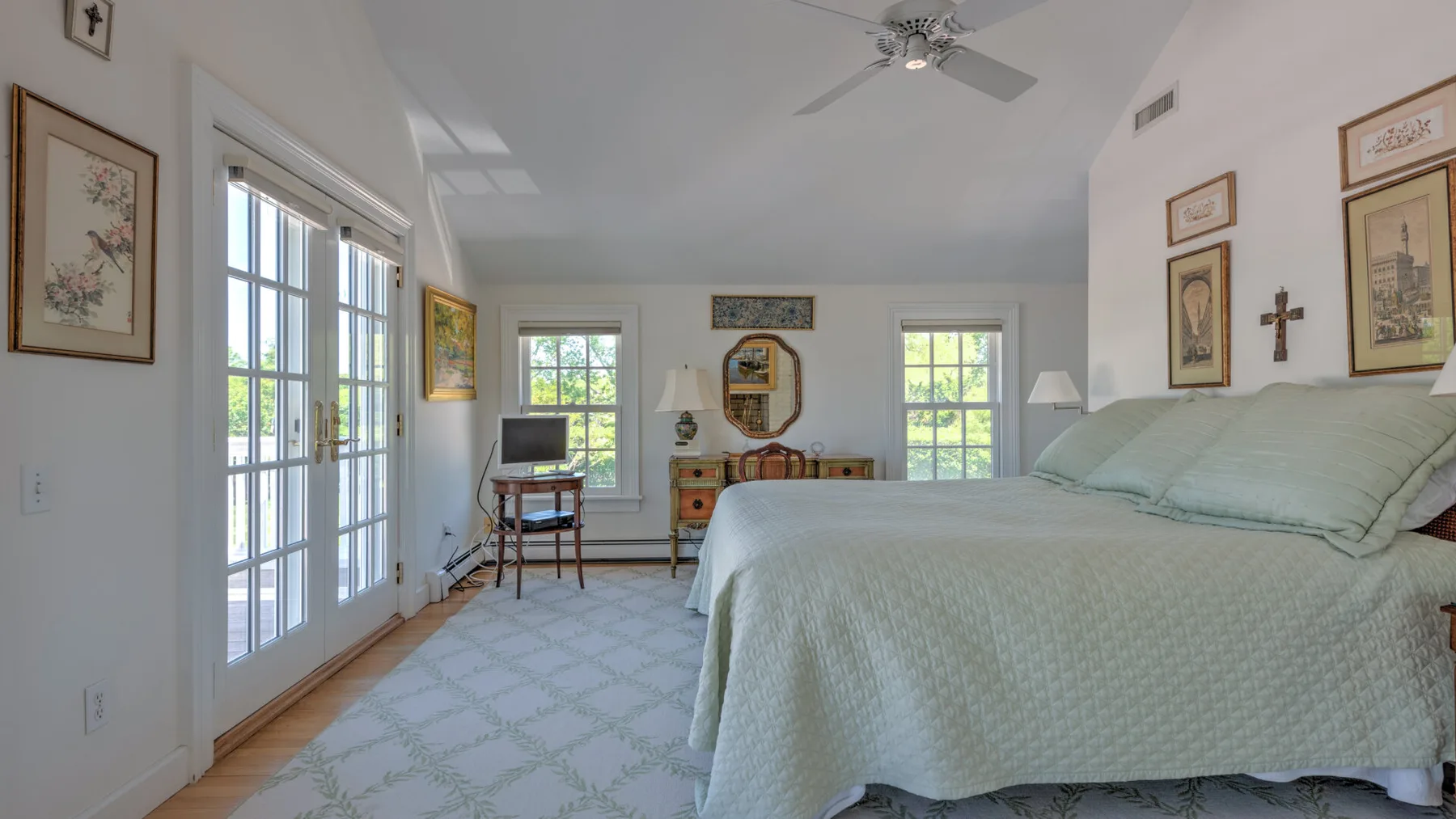 A bright bedroom with a large bed, framed artwork, and windows.