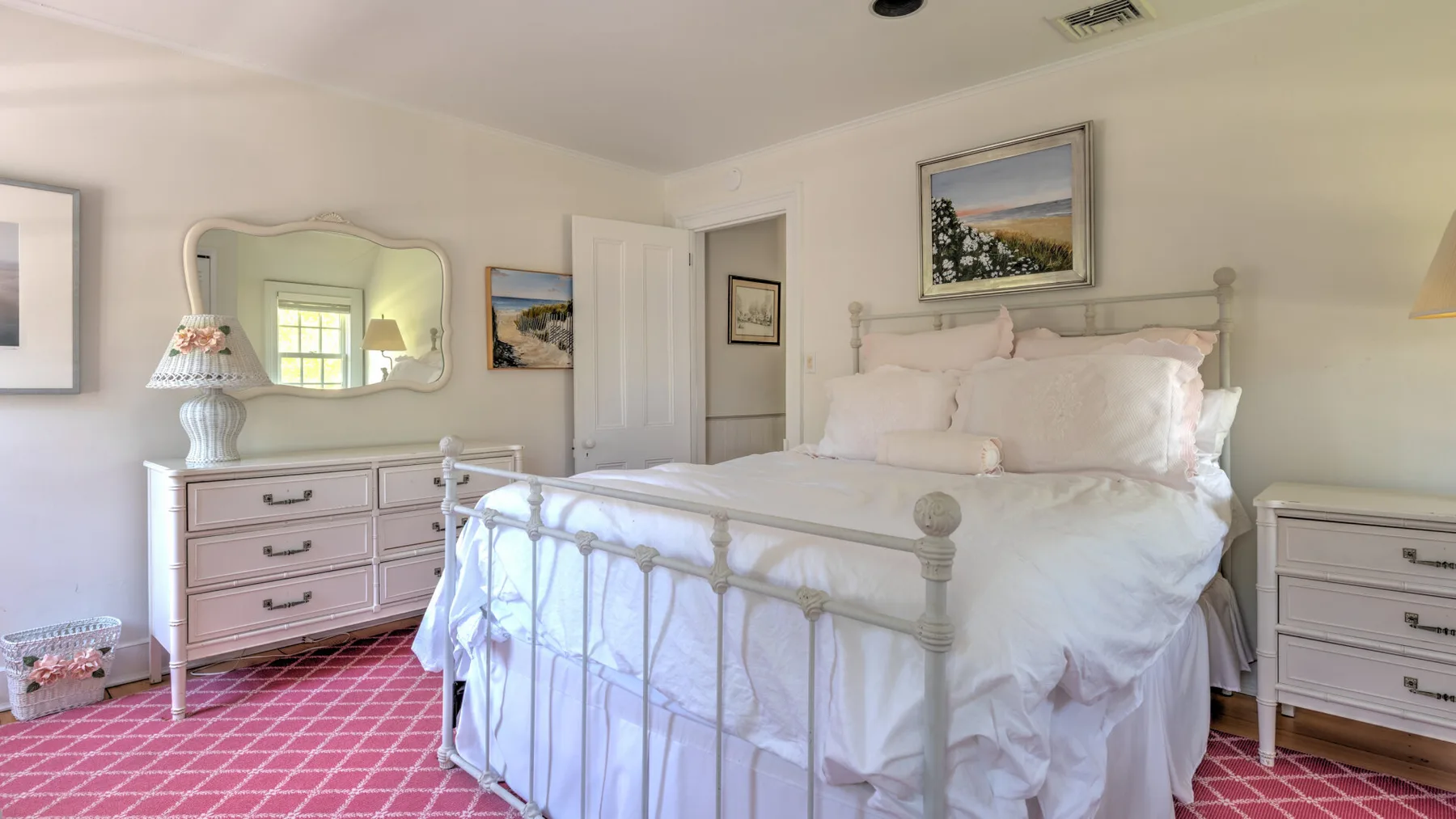 A bedroom with a large bed, bedside furniture, and framed pictures.