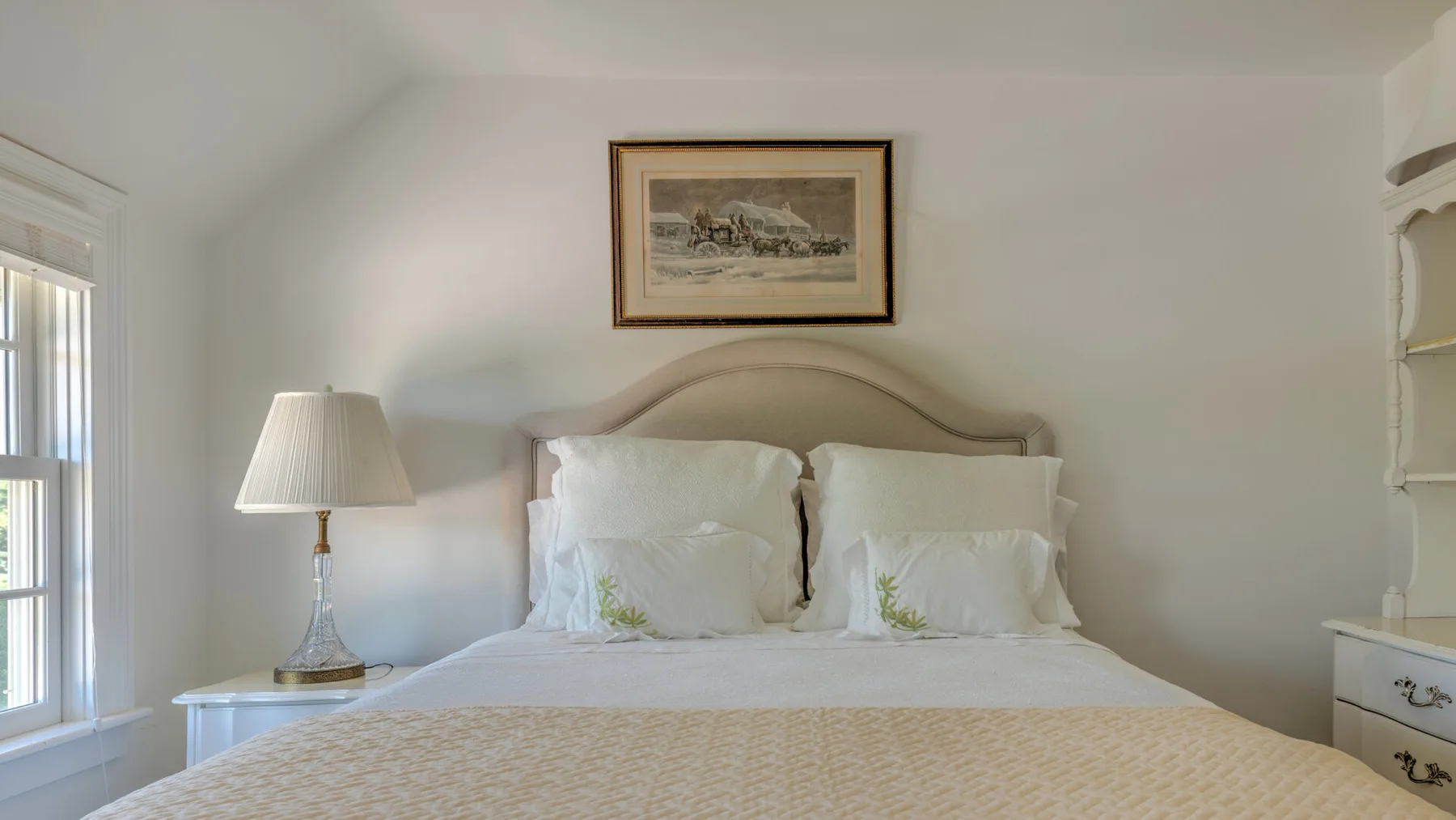 A bright bedroom with a neatly made bed and framed artwork above the headboard.