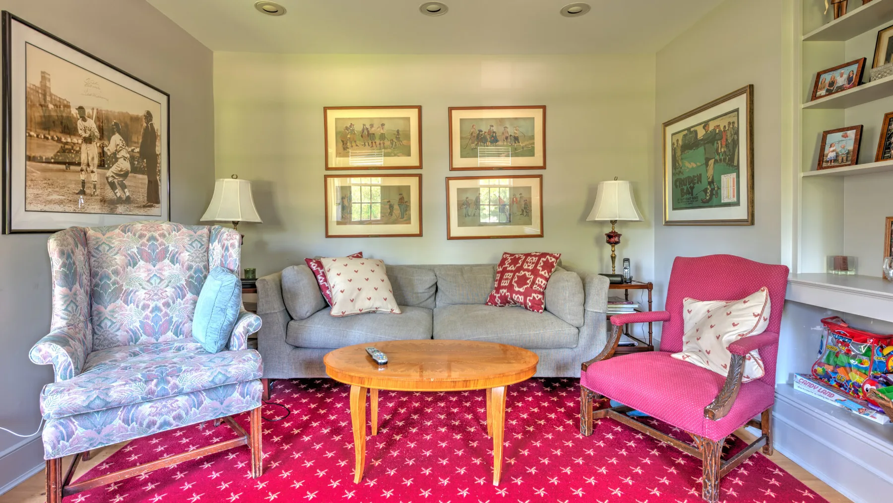 A living room with a gray sofa, colorful chairs, and a round wooden table.