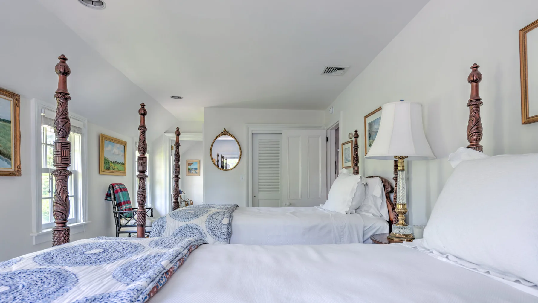 A bright bedroom with white bedding and tall carved bedposts.