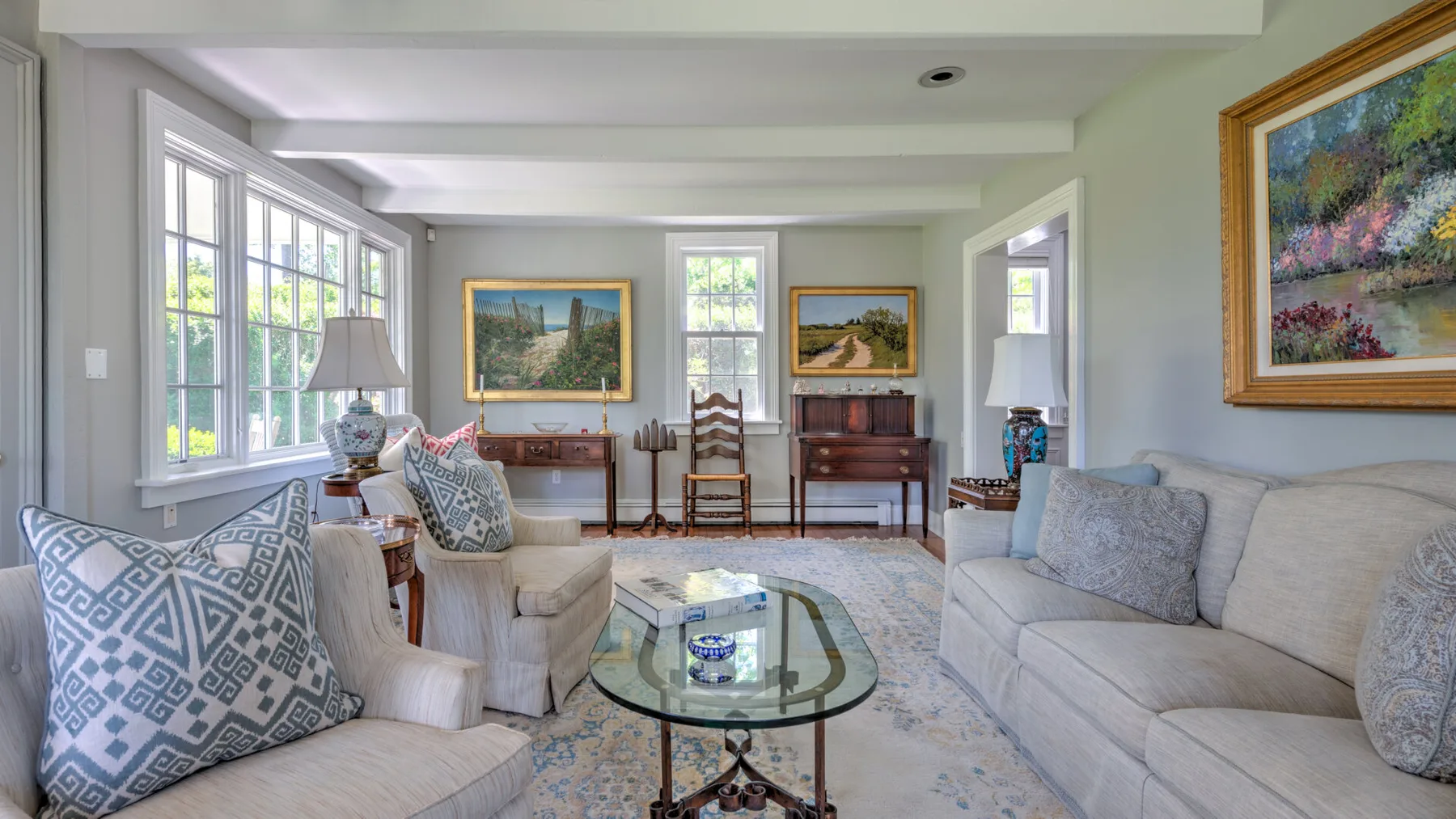 A bright living room with seating, a glass coffee table, and large windows.