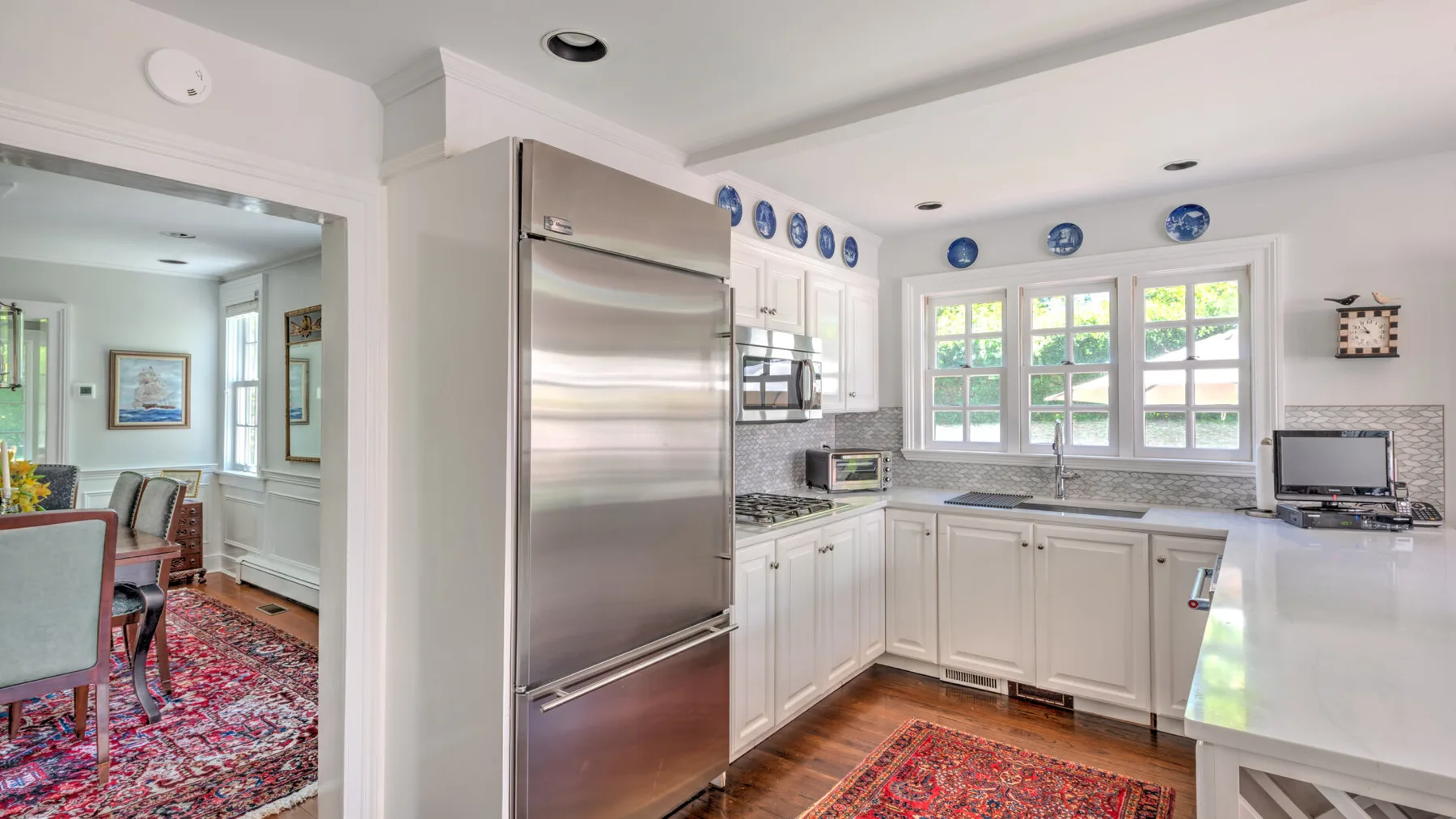 A bright kitchen with white cabinets, a stainless-steel refrigerator, and windows.