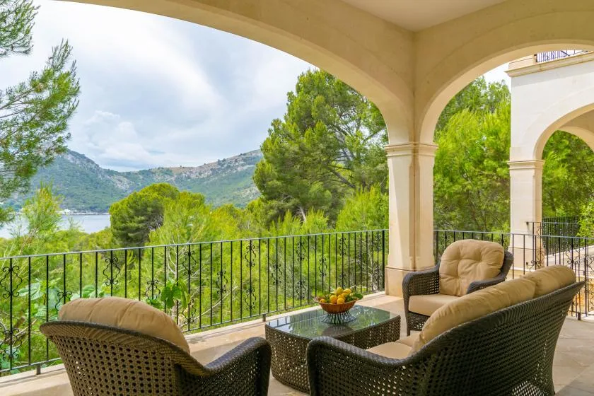 A covered terrace with seating overlooks trees, hills, and a lake.