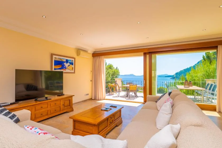 A bright living room opens onto a balcony with seating and a view of the water.