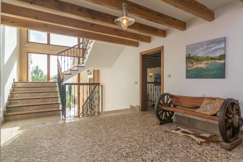 A bright stair hall with exposed wooden beams and a rustic bench.