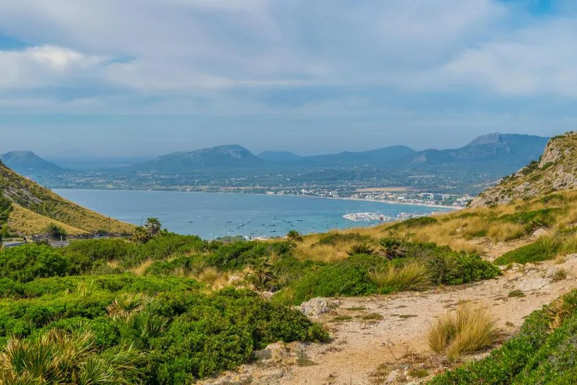 A coastal landscape with a bay, distant mountains, and a sandy trail.