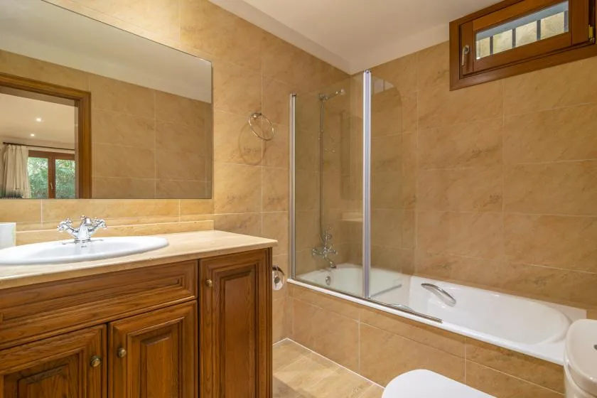 A bathroom with a vanity, mirror, and bathtub with a glass shower screen.