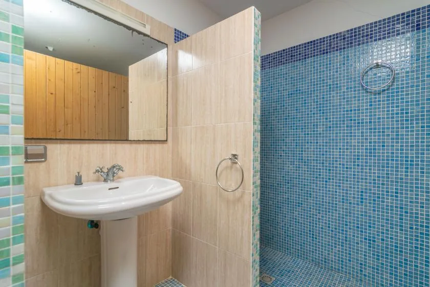 A tiled bathroom with a sink, mirror, and blue-tiled shower area.