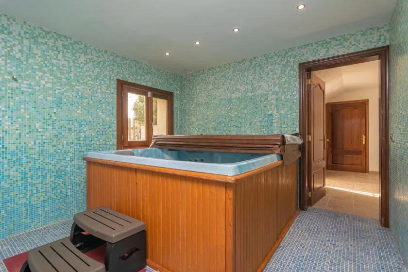 A tiled room with a large wooden hot tub and a window.