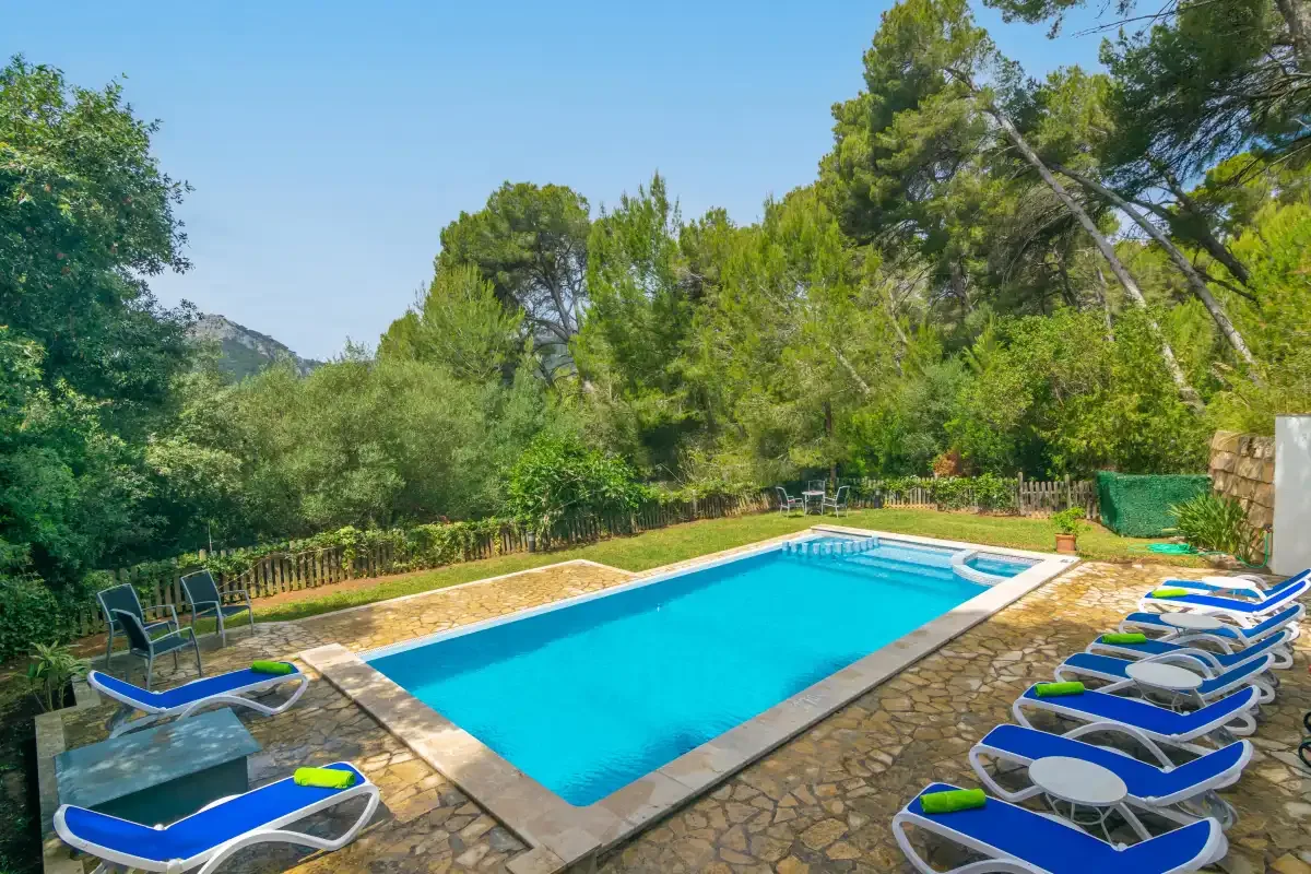 An outdoor swimming pool sits among trees, with loungers arranged along the stone patio.