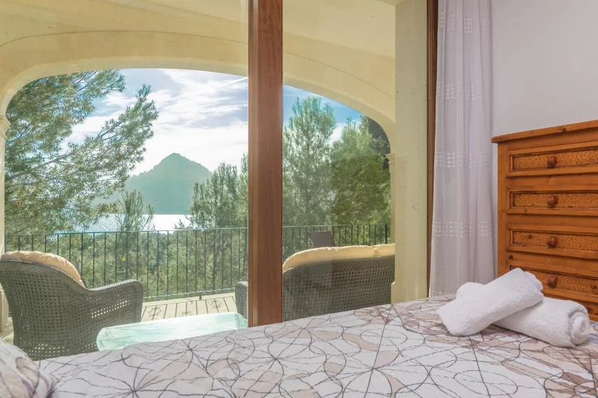 A bedroom opens onto a balcony overlooking trees and a distant mountain.