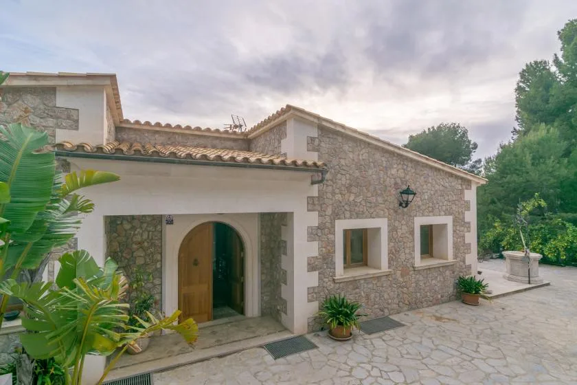A stone house exterior with an arched wooden entrance and paved courtyard.