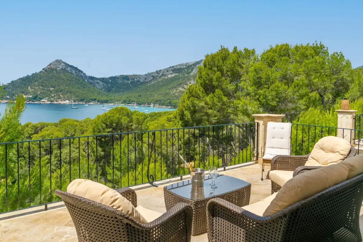 A terrace seating area overlooks a bay, green hills, and trees.