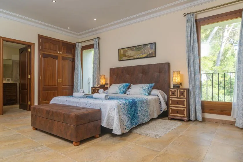 A bedroom with a bed, bedside tables, and a large window overlooking greenery.