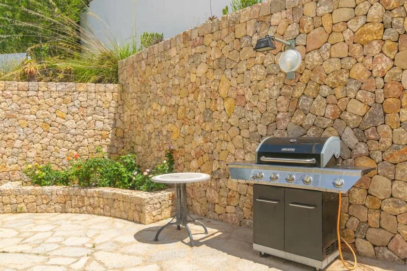 An outdoor patio with a barbecue grill beside a stone wall.