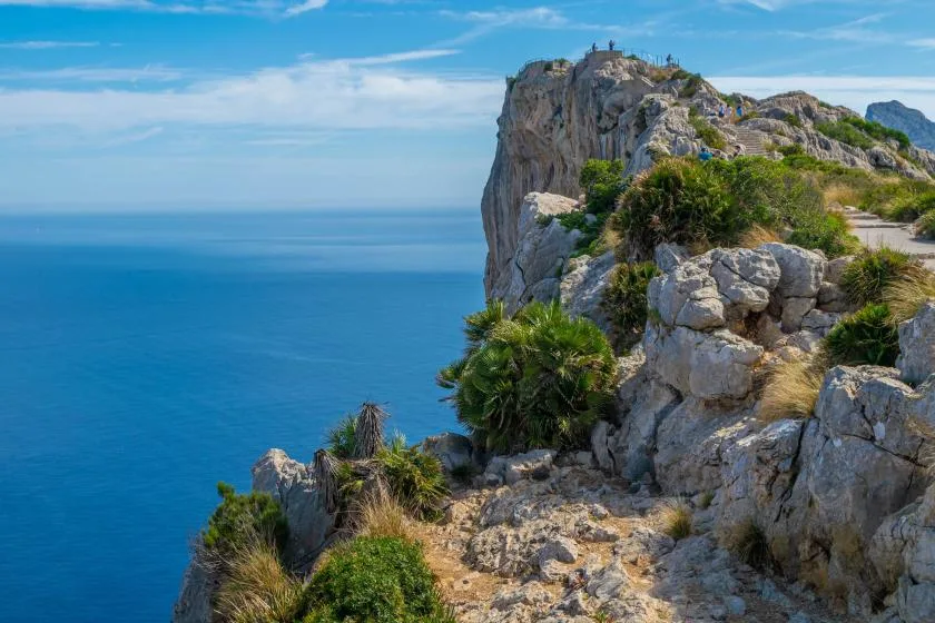A rocky coastal path winds past rugged cliffs overlooking the blue sea.