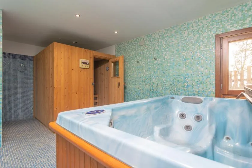 A tiled spa room with a large built-in soaking tub beside a wooden sauna.