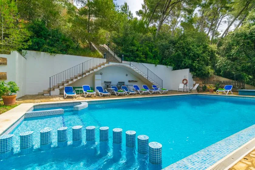 Piscina al aire libre con agua azul, tumbonas y una escalera detrás.
