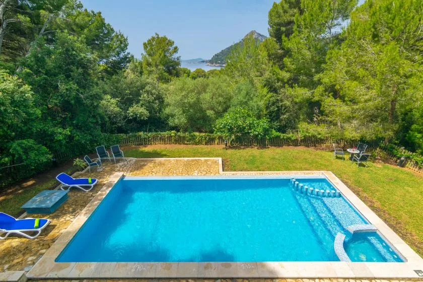 Una piscina al aire libre está rodeada de árboles, con el mar a lo lejos.