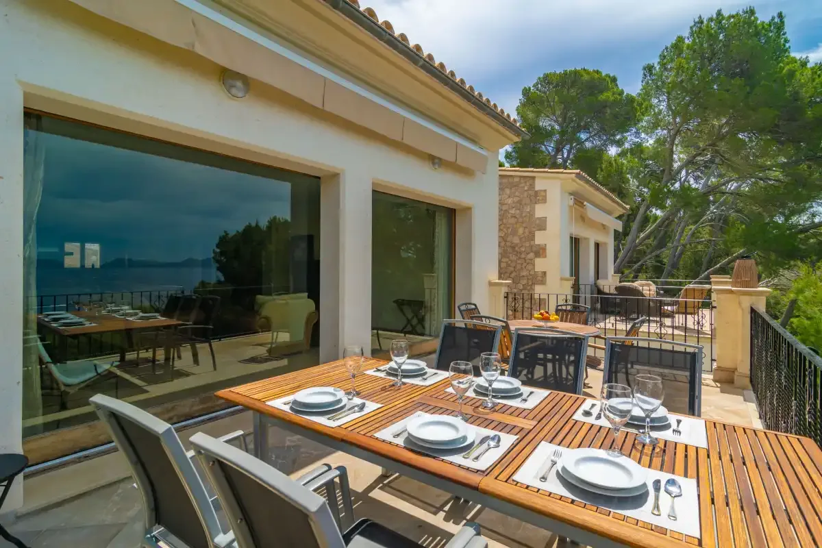 An outdoor dining terrace with a set table beside large glass doors.
