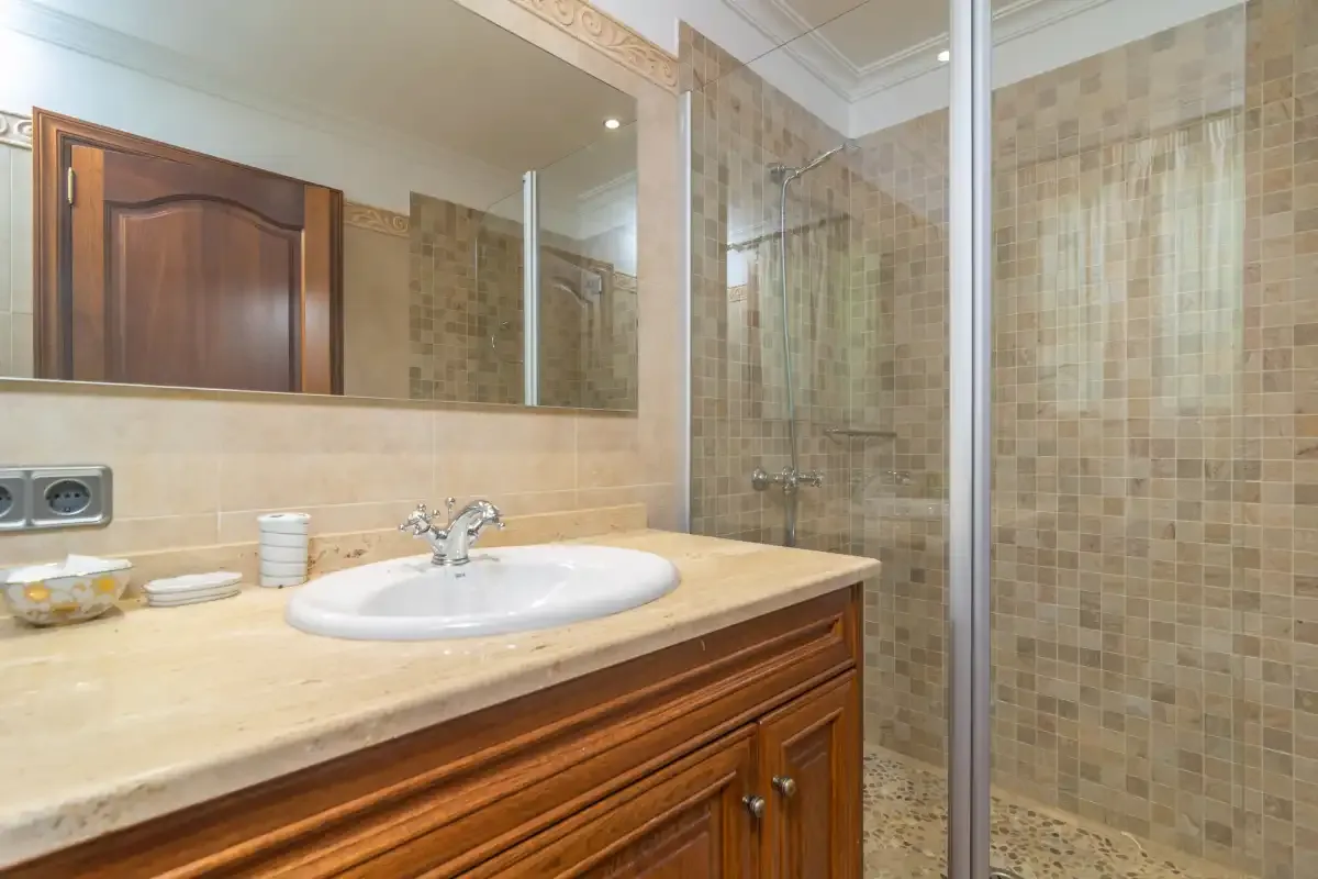 A bathroom with a sink, wooden vanity, and tiled shower.