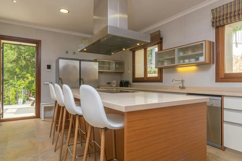 A modern kitchen with a large island and white bar stools.