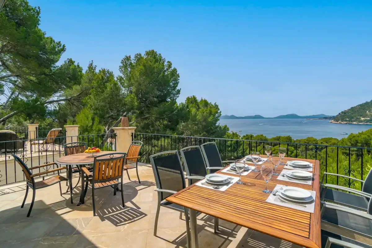 An outdoor dining terrace overlooks a bay, with tables and seating in the foreground.