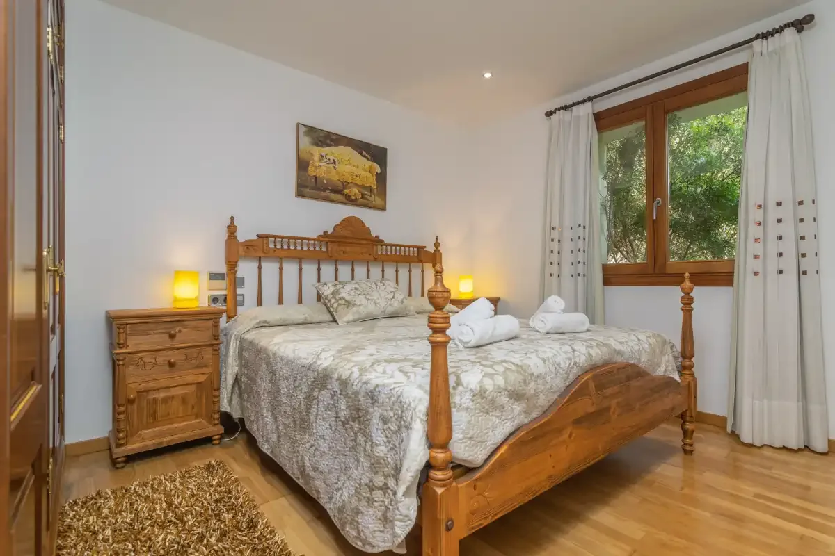 A bedroom with a wooden bed and a window overlooking greenery.