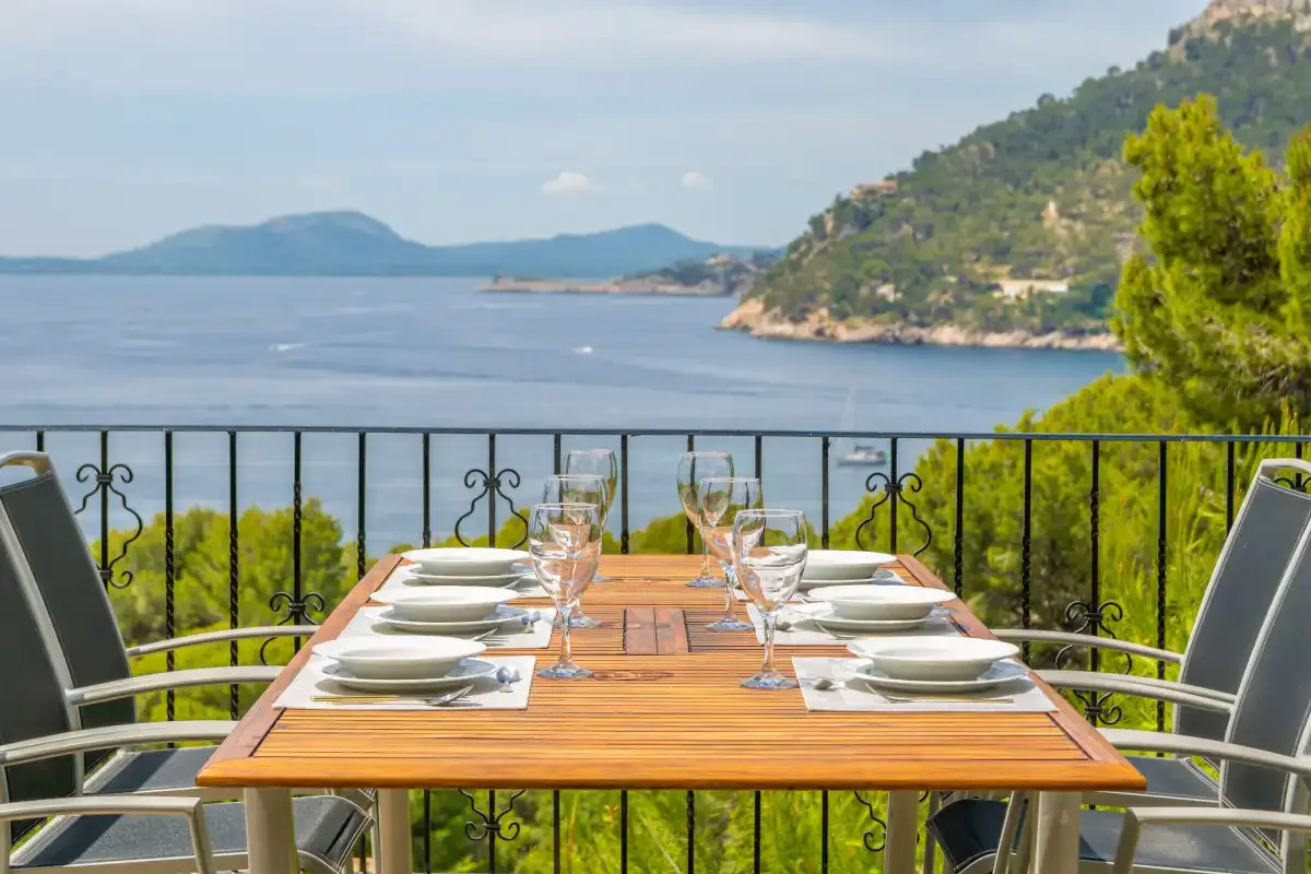 A balcony dining table is set beside a railing overlooking the sea.