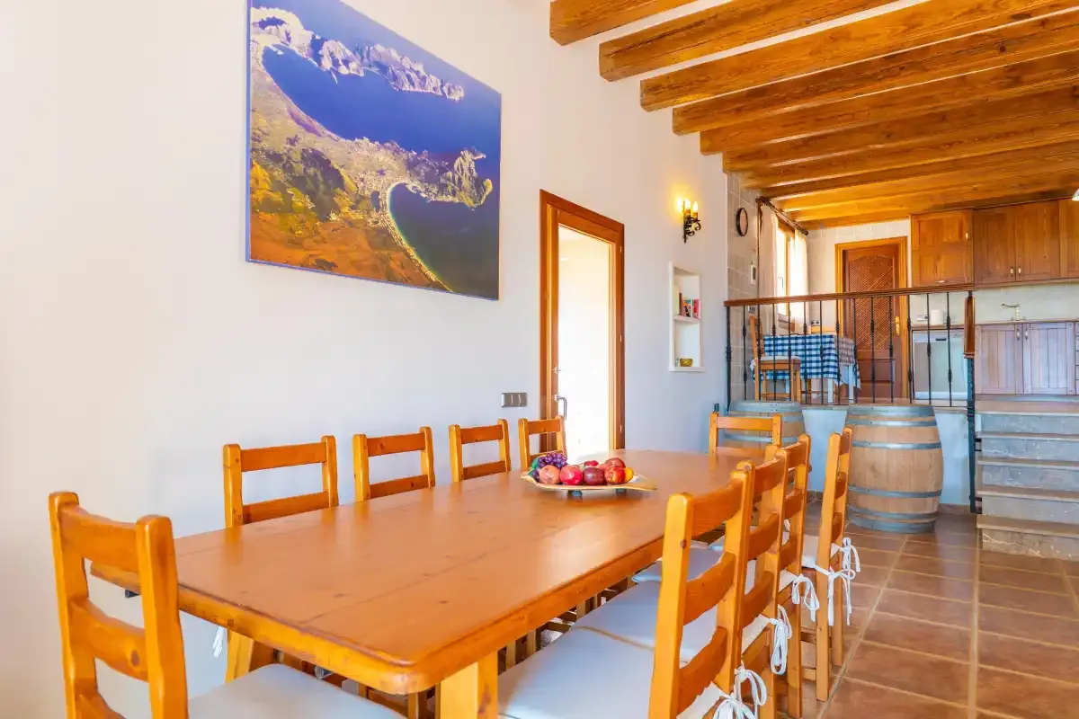 A dining room with a long wooden table and chairs beneath exposed ceiling beams.