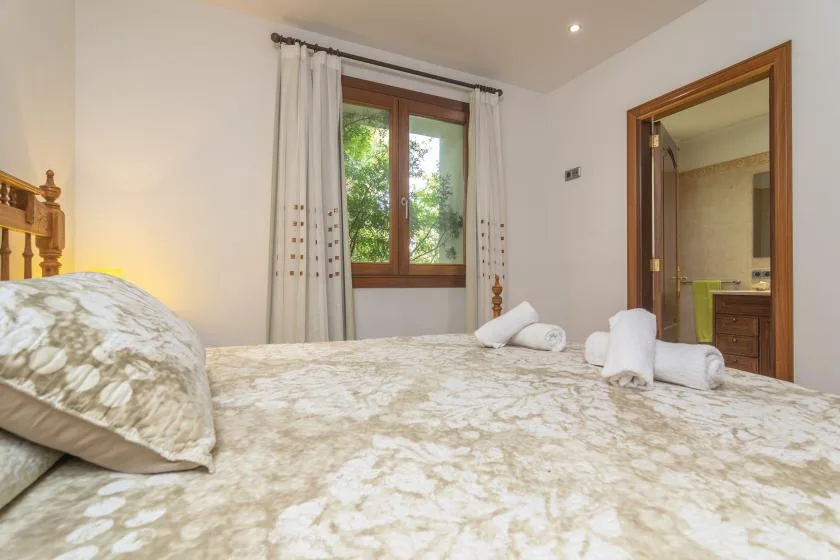 A bedroom with a patterned bedspread, curtained window, and doorway to a bathroom.