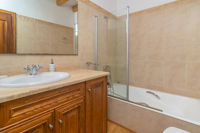 A bathroom with a wooden vanity, sink, and bathtub with a glass shower screen.