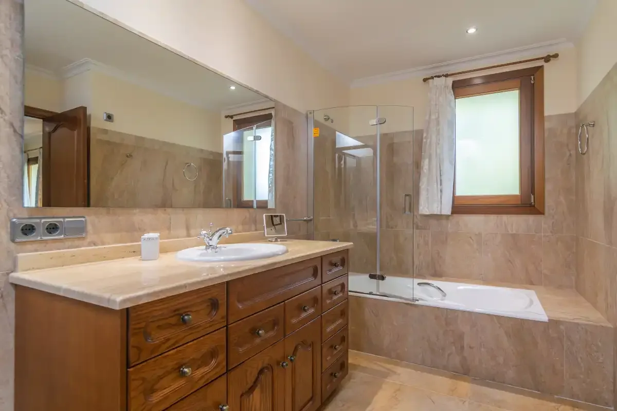 A bathroom with a wooden vanity, a bathtub, and a window.