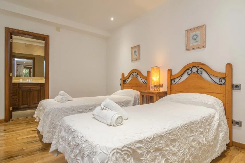 A bedroom with two beds dressed in white linens and a wooden bedside table.