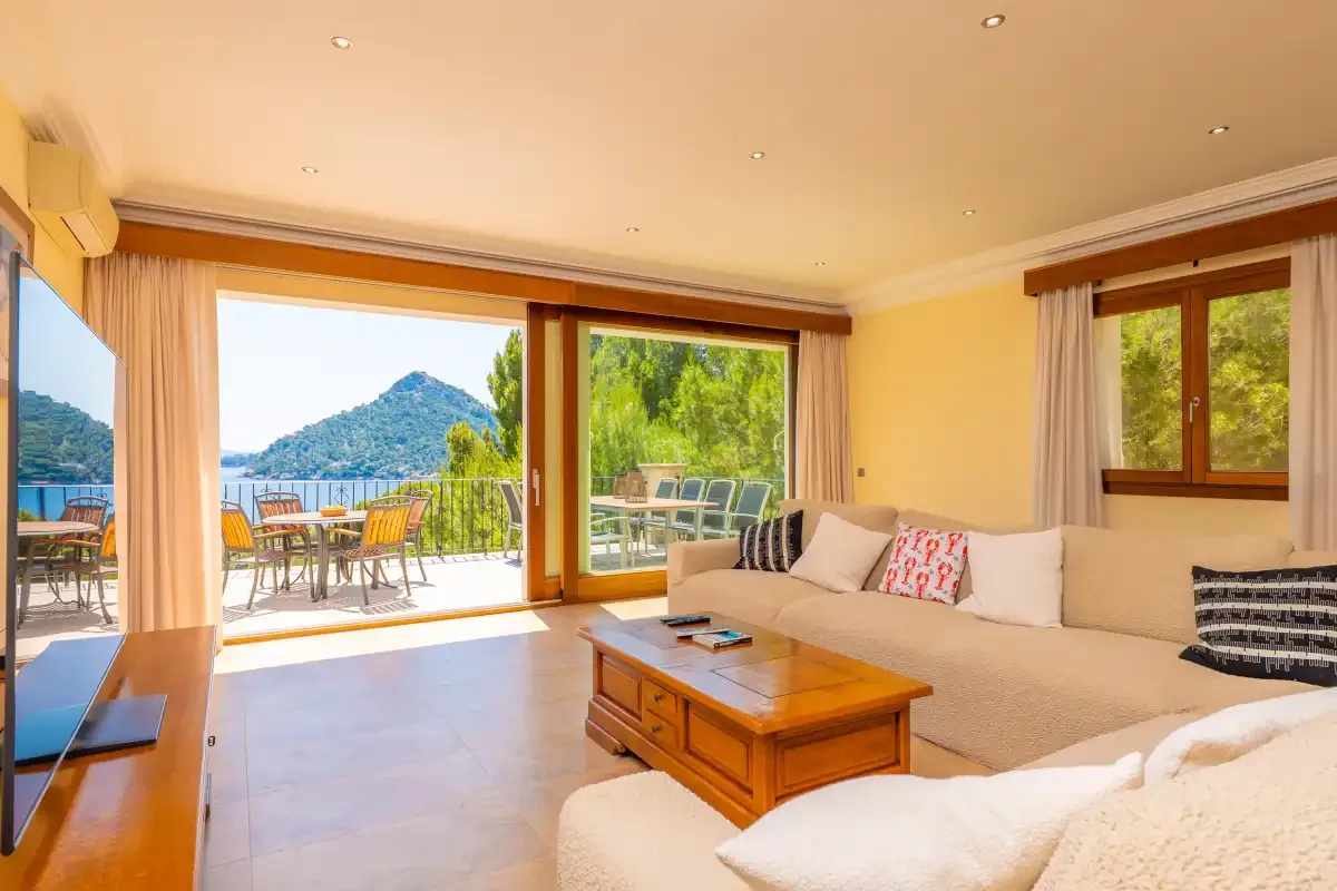 A bright living room opens onto a terrace with seating and a mountain view.