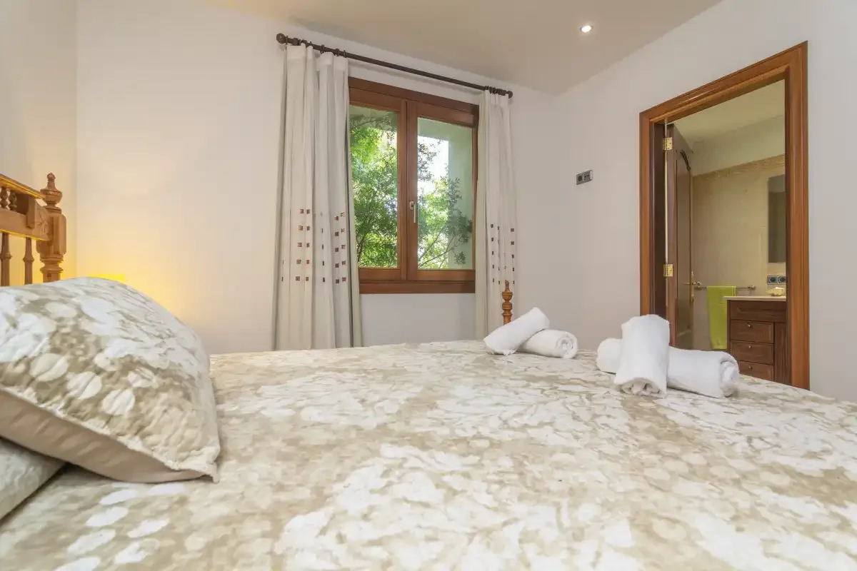 A bedroom with a bed, folded towels, and a window overlooking greenery.
