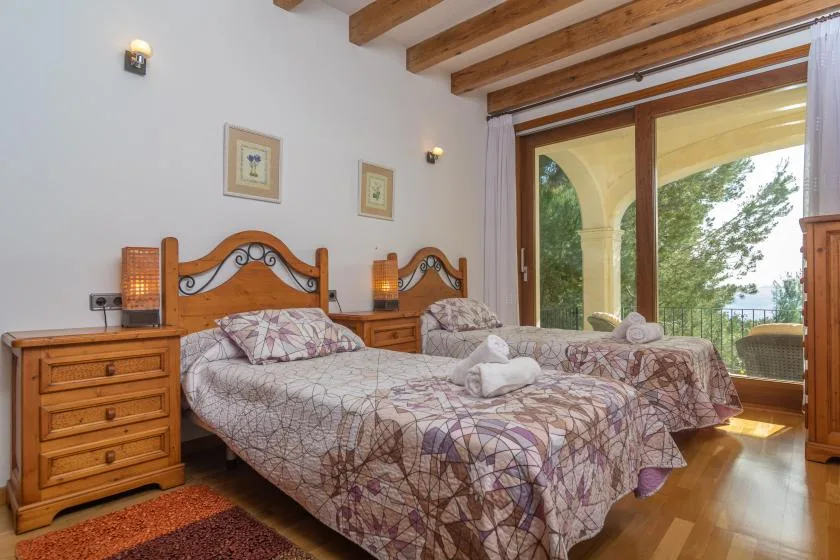 A bedroom with two beds, wooden furnishings, and glass doors opening to a balcony.